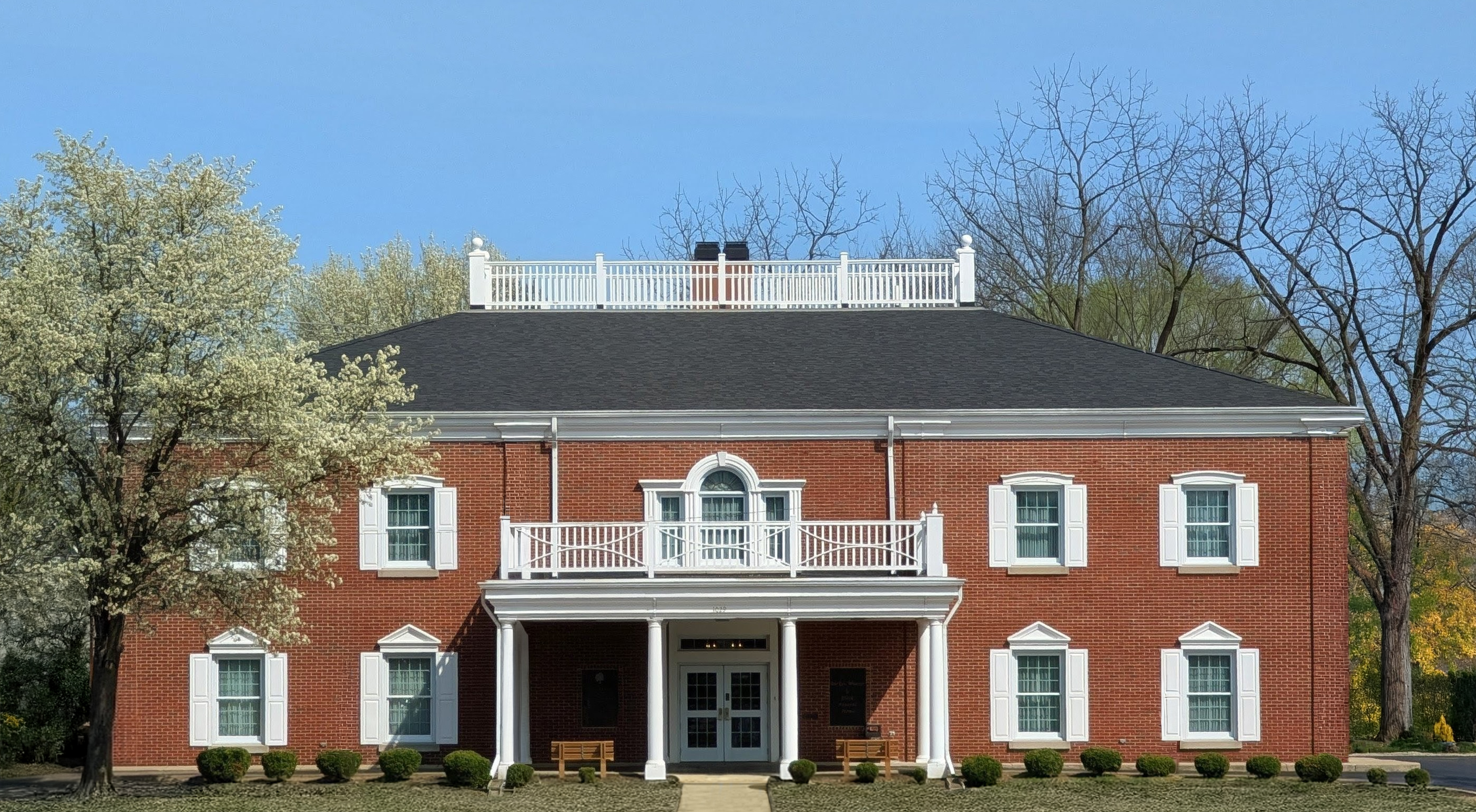 Front exterior of Downtown Funeral Home building with white columns, balcony, and landscaped entrance.&rdquo;